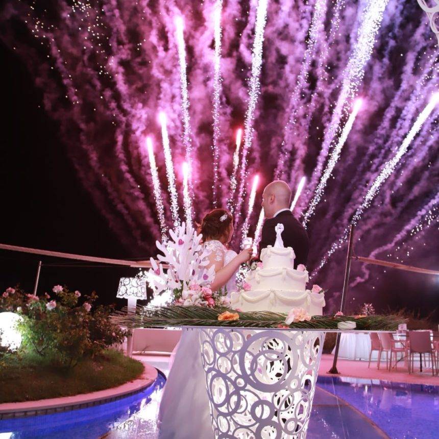 Gli sposi tagliano la torta a bordo piscina, con i fuochi d’artificio sullo sfondo
